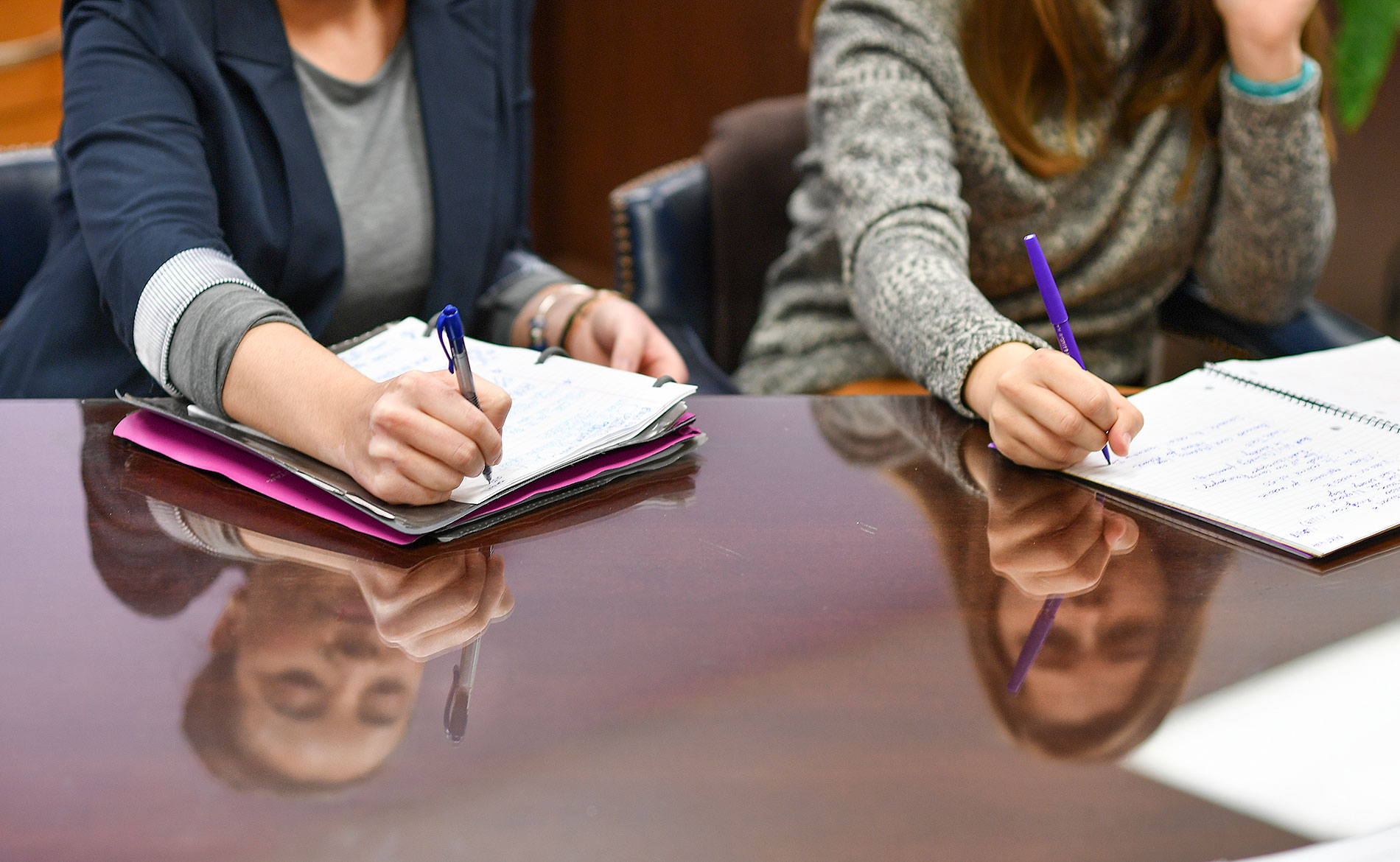 Students writing in notebooks with reflection on desk