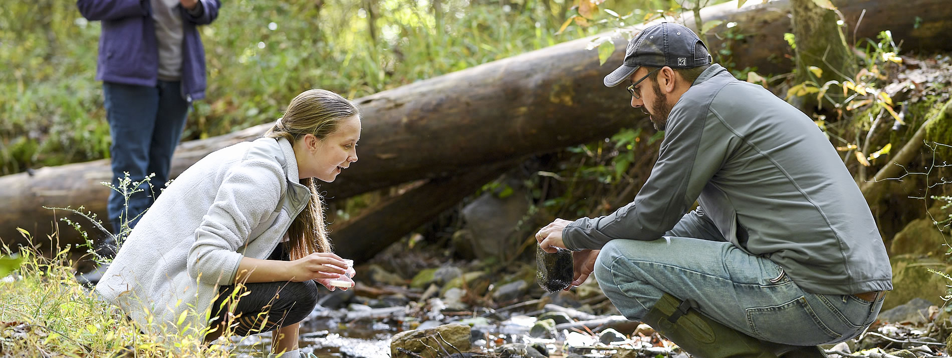 A female student and a male professor crouching over a river, conversing